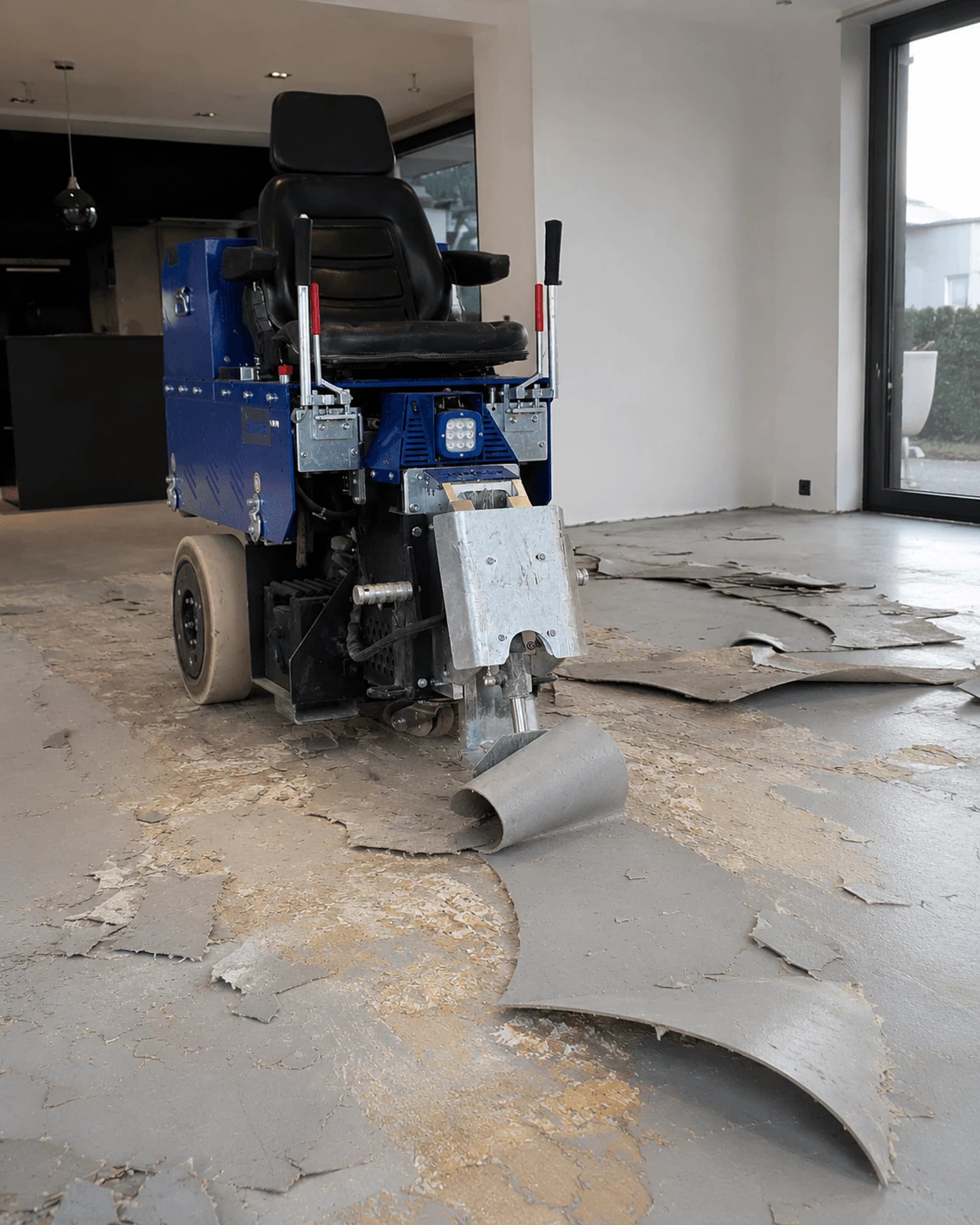 Machine met stoel verwijdert oude vloerbedekking in een lege kamer met grote ramen