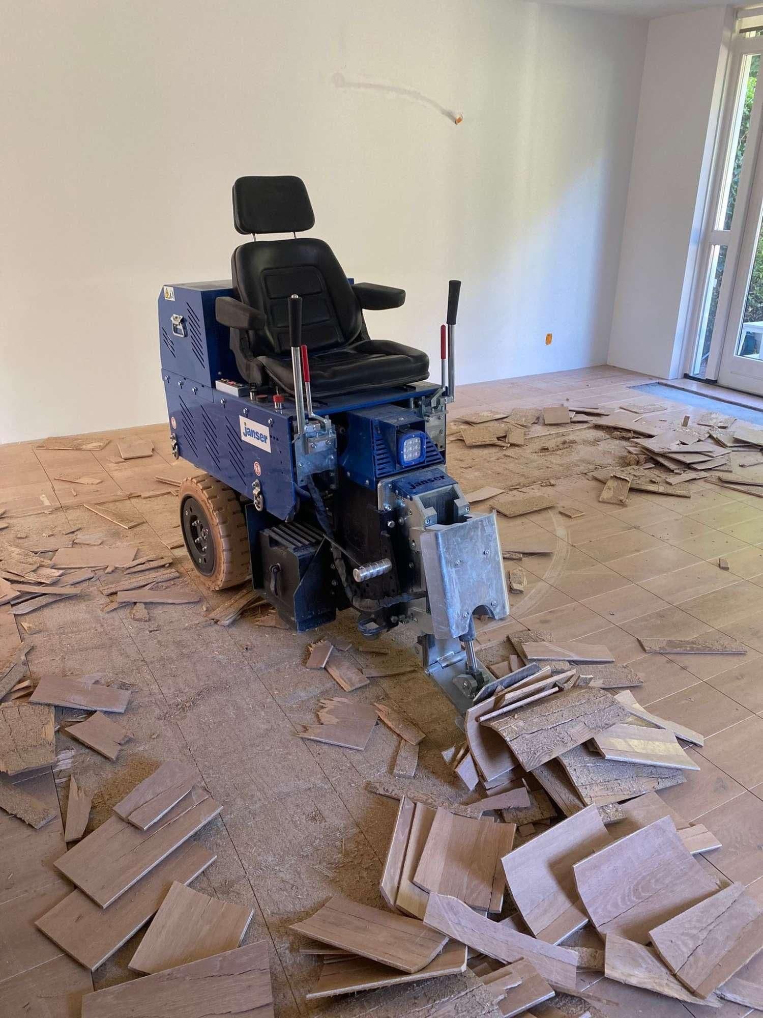 Elektrische vloerstripmachine met stoel en handgrepen in ruimte met houten vloerdeelstukken op de grond
