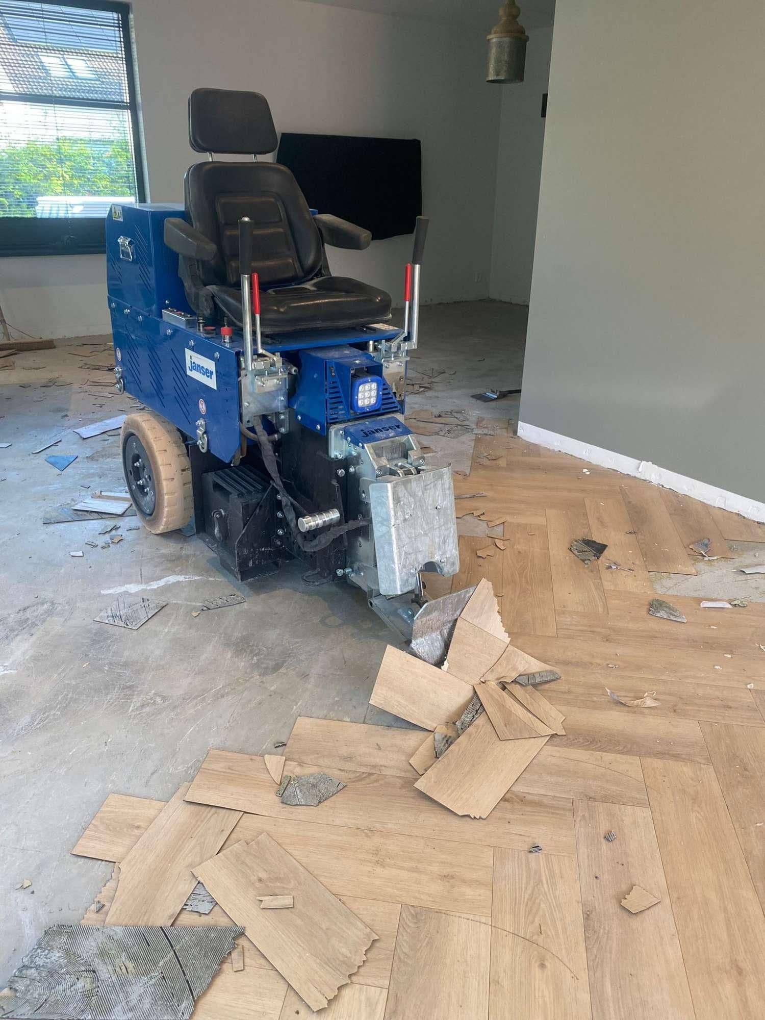 Blauwe machine met stoel die houten vloerplanken verwijdert in een lege ruimte