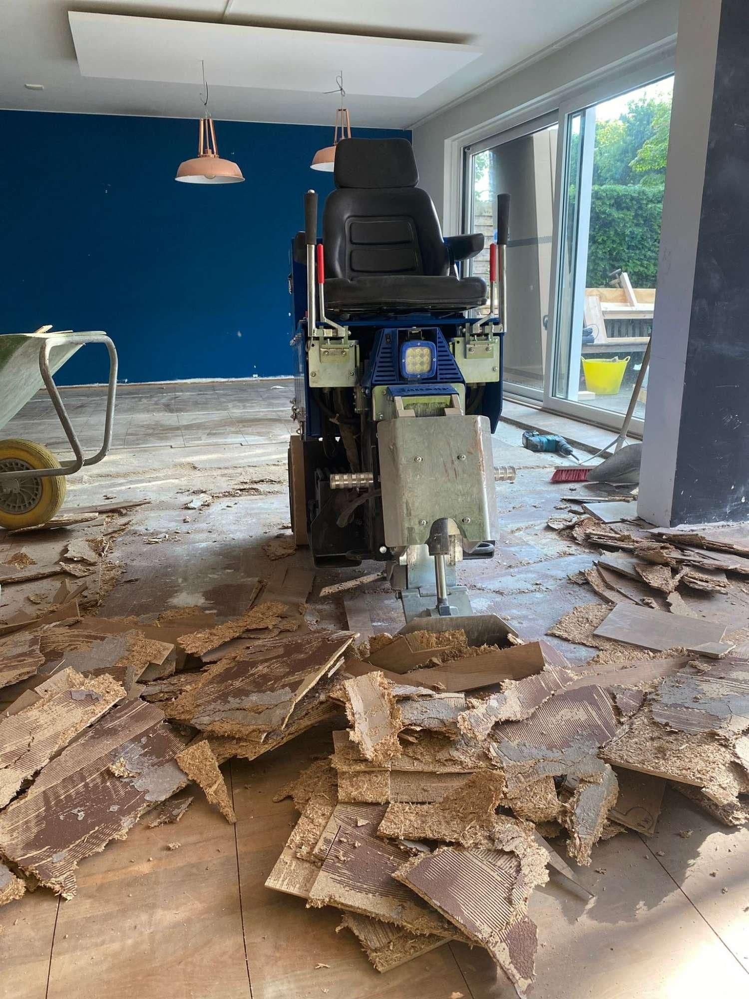 Machine die houten vloerbedekking verwijdert in een binnenruimte met blauwe muur en grote ramen
