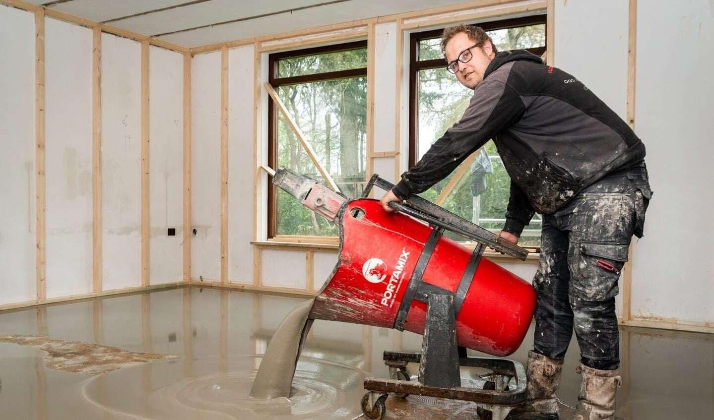 Man die met een rode mengmachine vloeibare cementvloer in een kamer stort