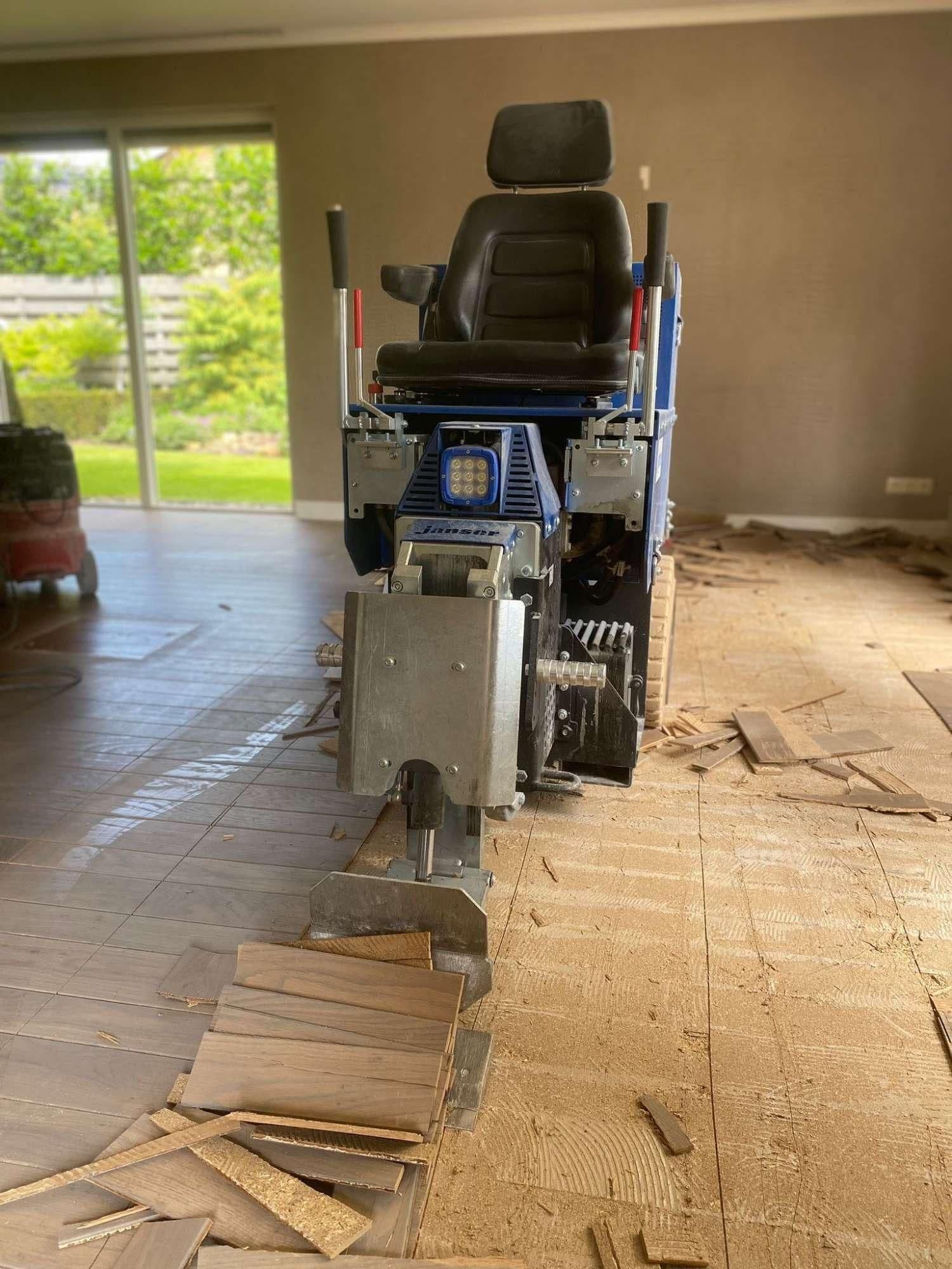 Machine met zitplaats die houten vloer verwijdert in een binnenruimte met schuifdeuren naar buiten.